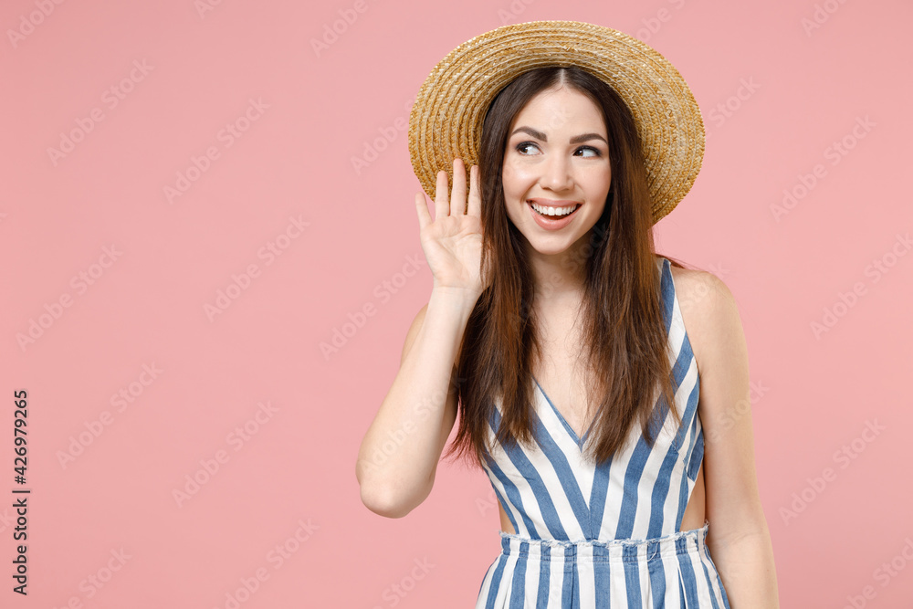 Young curious nosy smiling woman 20s wearing summer clothes striped dress straw hat try to hear you overhear listening intently isolated on pastel pink background studio. People lifestyle concept. Young curious nosy smiling woman 20s wearing summer clothes striped dress straw hat try to hear you overhear listening intently isolated on pastel pink background studio. People lifestyle concept.