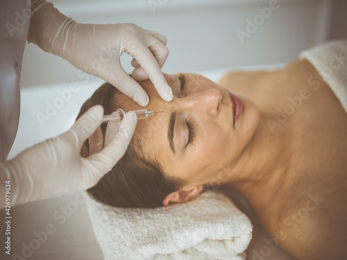 Beautician doing beauty procedure with syringe to face of young brunette woman. Cosmetic medicine and surgery  beauty injections