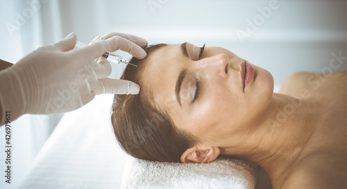 Beautician doing beauty procedure with syringe to face of young brunette woman. Cosmetic medicine and surgery, beauty injections