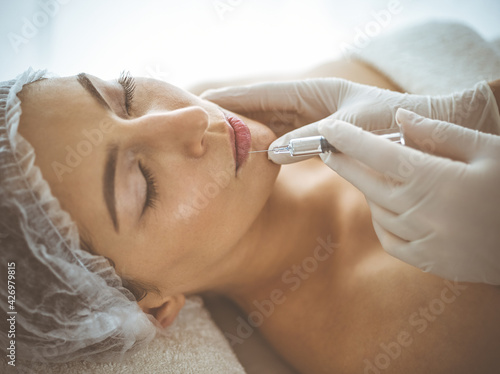 Beautician doing beauty procedure with syringe to face of young brunette woman. Cosmetic medicine and surgery  beauty injections