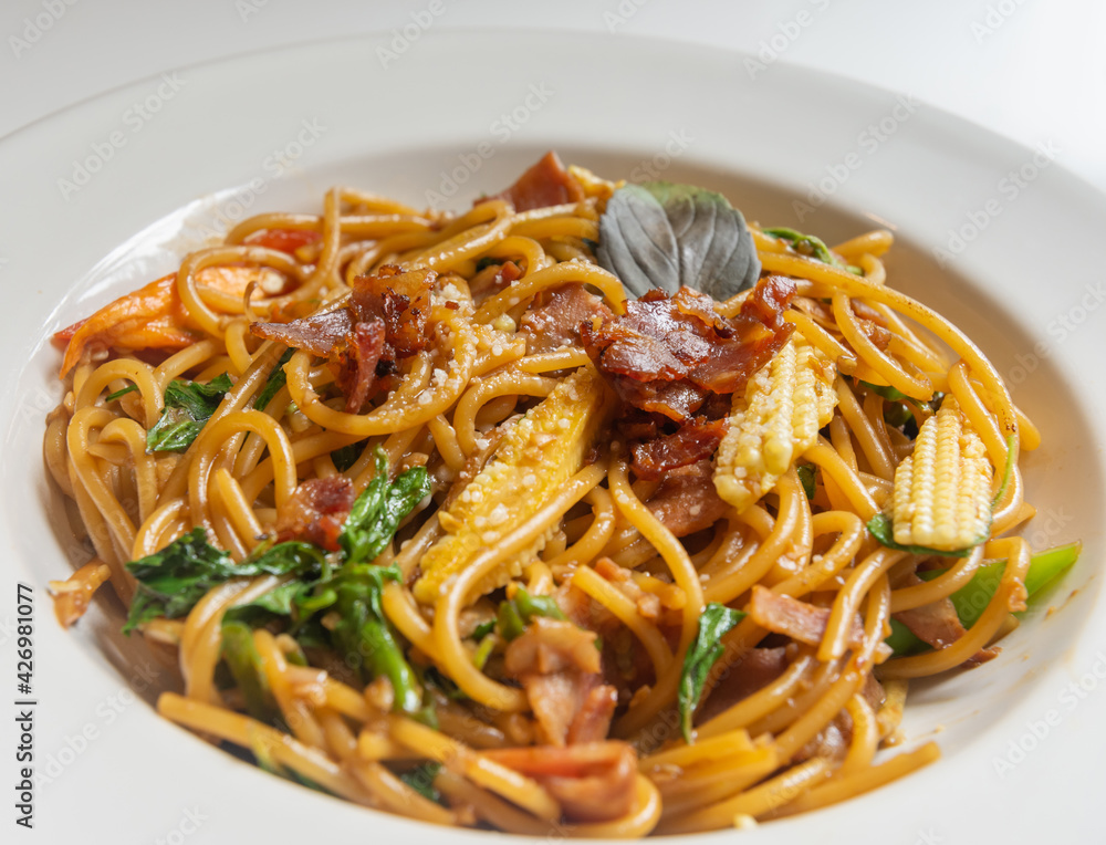Spicy spaghetti with bacon and basil in the white dish.
