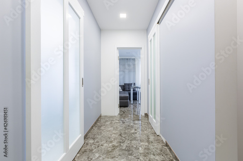 Interior photography, corridor of a small apartment in a modern minimalist style, with white walls, sliding doors, and black marble tiles on the floor