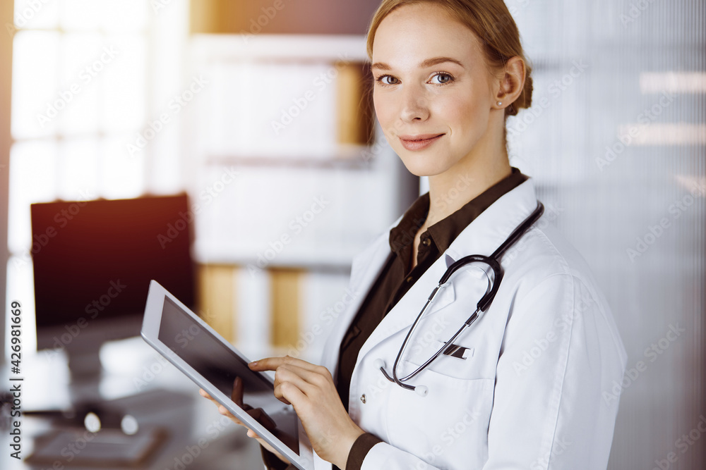 Cheerful smiling female doctor using clipboard in clinic. Portrait of friendly physician woman at work. Medical service in hospital. Medicine concept Cheerful smiling female doctor using clipboard in clinic. Portrait of friendly physician woman at work. Medical service in hospital. Medicine concept