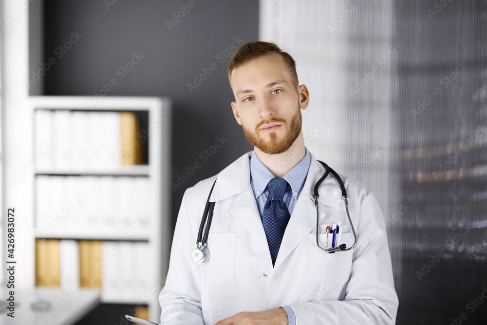 Friendly red-bearded doctor using tablet computer in clinic. Perfect medical service in hospital and medicine concept Friendly red-bearded doctor using tablet computer in clinic. Perfect medical service in hospital and medicine concept
