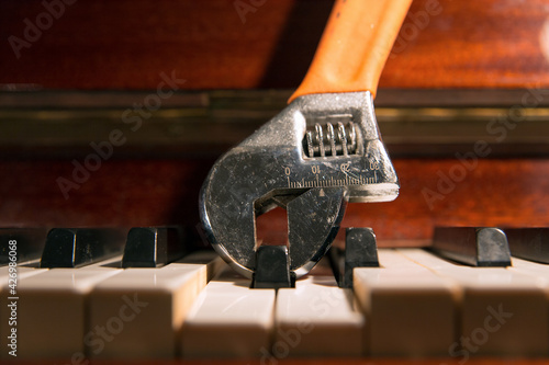 Close up of an adjustable wrench holding and pressing a piano key. Fine tuning concept.
