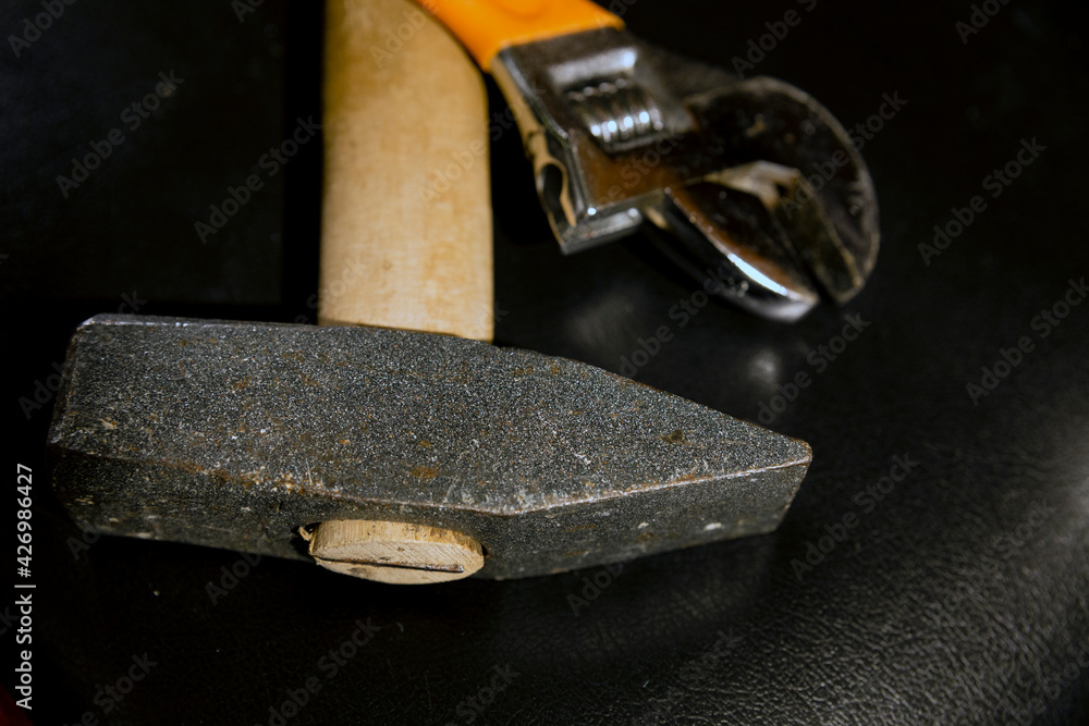 Selective focus on the head of a hammer which is accompanied by an adjustable wrench lying on a leather surface. Selective focus on the head of a hammer which is accompanied by an adjustable wrench lying on a leather surface.