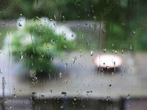 Rain drops on glass window with green blurred background of garden