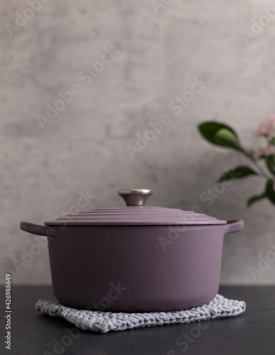 Round lilac rustic cast iron casserole on a knitted blue cloth over a gray background. photo