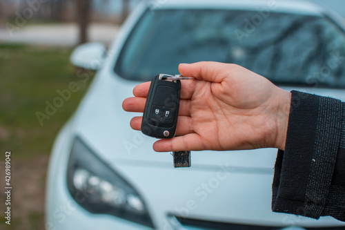Close up hand of Woman holding car key with blurred car on background.