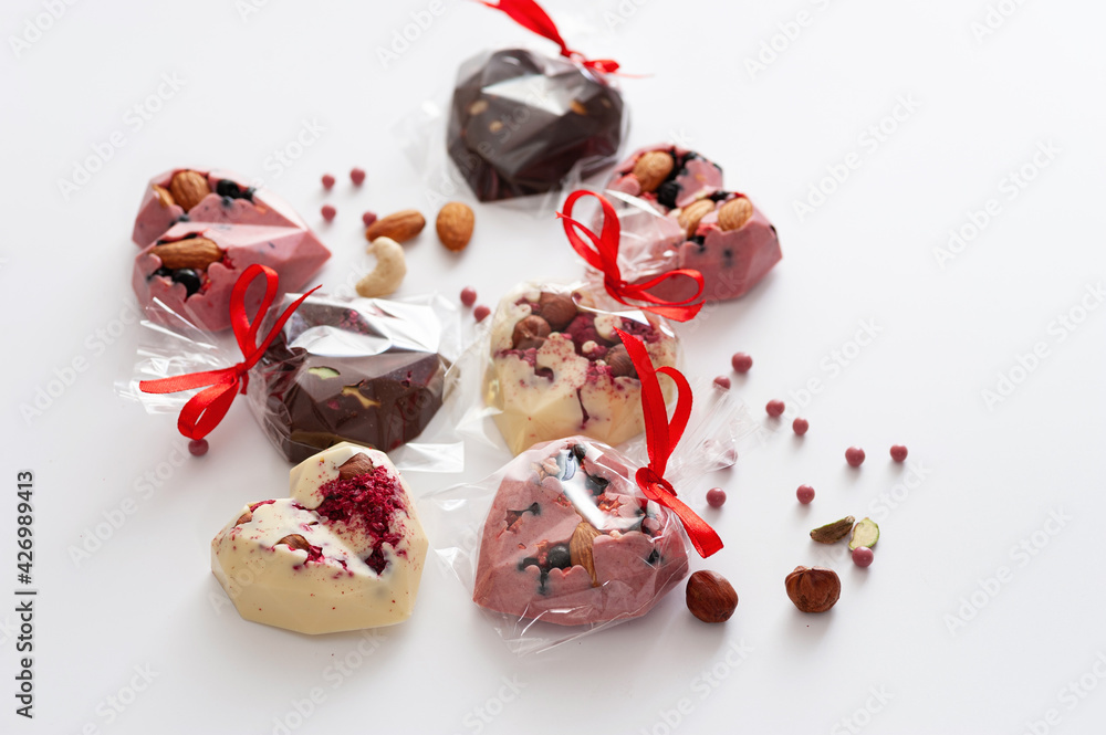chocolates mix, in the form of hearts with pink, milk and white chocolate with strawberries, blueberries and almonds, tied with a ribbon, handmade, top view, on a white background chocolates mix, in the form of hearts with pink, milk and white chocolate with strawberries, blueberries and almonds, tied with a ribbon, handmade, top view, on a white background