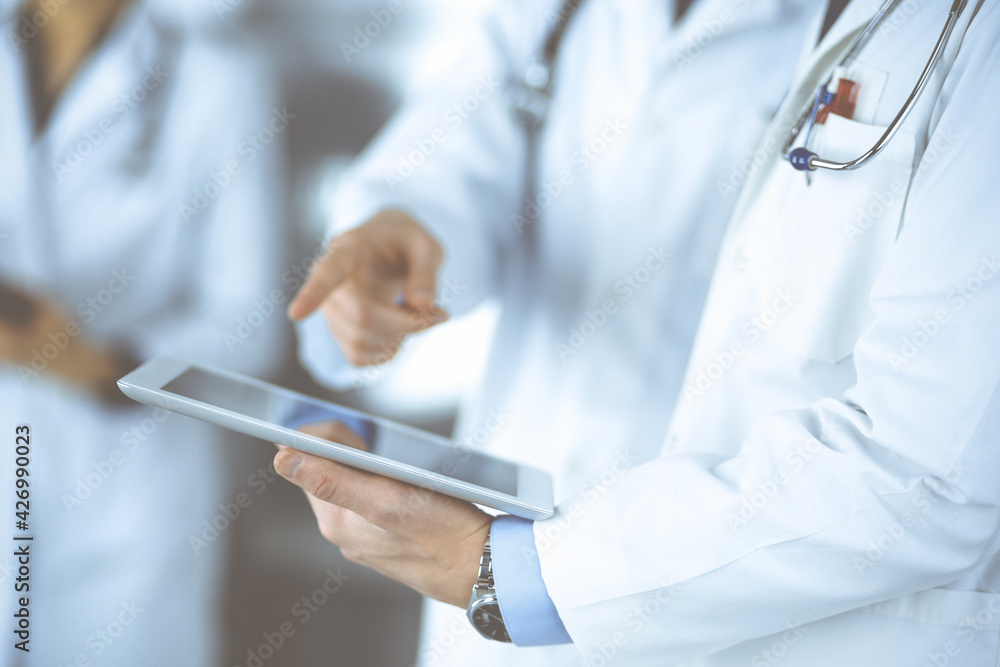 Group of unknown doctors use a computer tablet to check up some medical names records, while standing in a hospital office. Physicians ready to examine and help patients. Medical help, insurance in Group of unknown doctors use a computer tablet to check up some medical names records, while standing in a hospital office. Physicians ready to examine and help patients. Medical help, insurance in