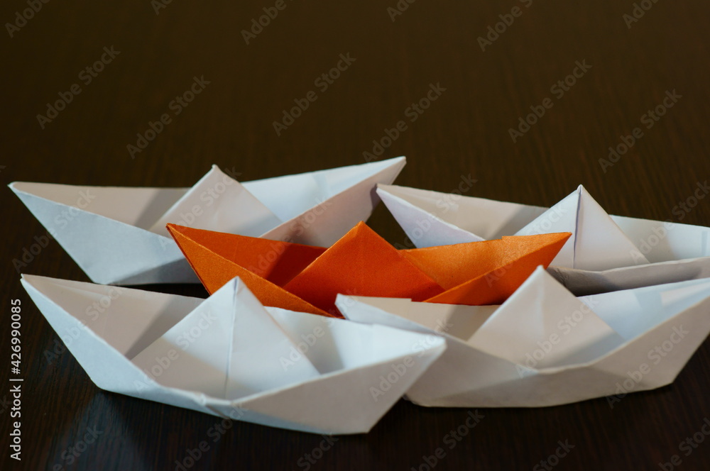Several paper boats on the table. One of them is orange. Several paper boats on the table. One of them is orange.