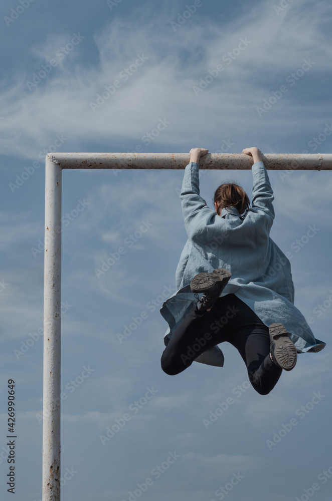 Woman jumping and grabbing a metal bar with hands, with sky as ...