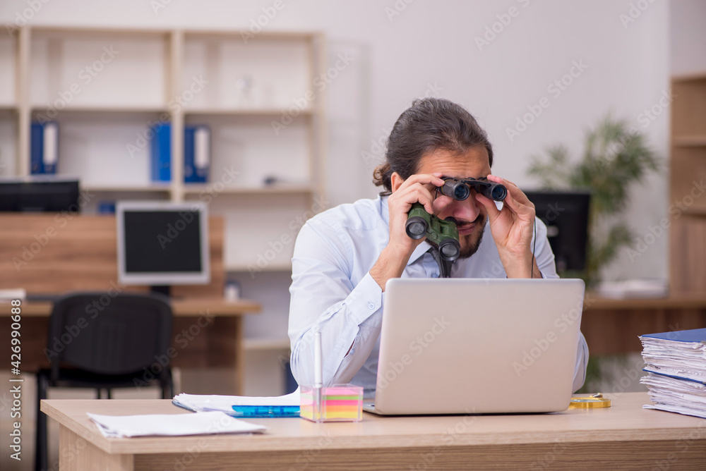 Young male employee holding binoculars in industrial espionage c Young male employee holding binoculars in industrial espionage c