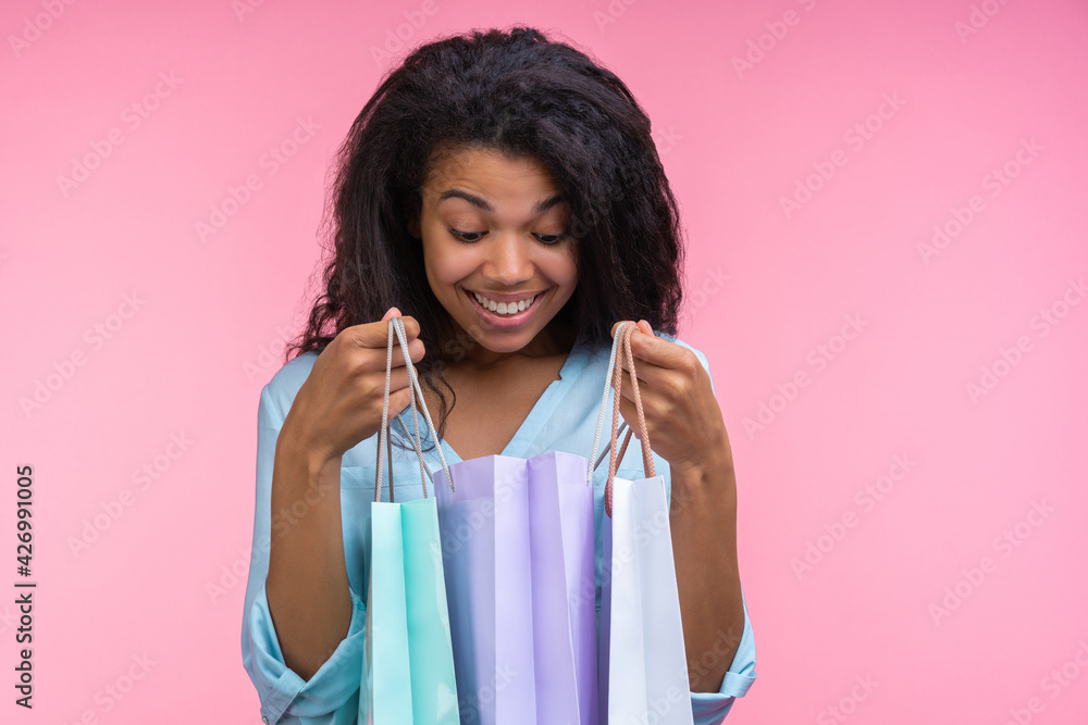 Smiling excited dark skinned girl looking into one of the shoping bags she's holding examining her purchase Smiling excited dark skinned girl looking into one of the shoping bags she's holding examining her purchase