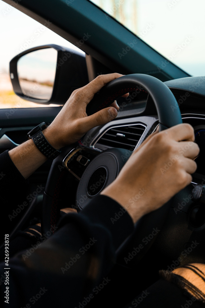 Close-up of hands holding the handlebars of a car, wearing a smart watch on the wrist. Wearing dark, modern clothes.