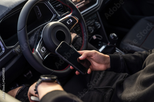 Unrecognisable man sitting in the pilot's seat using a mobile phone, wearing dark, modern clothes, holding the phone in one hand and a smart watch in the other. © J.Poquet