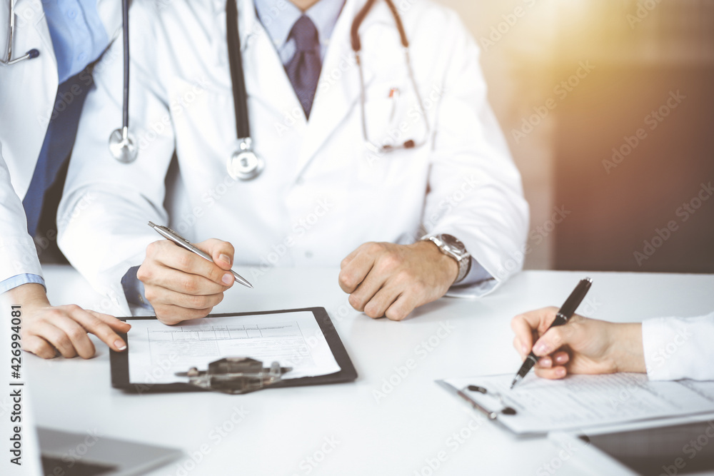 Group of unknown doctors are sitting at the desk and discussing problems or disease treatment in sunny hospital office. Covid 2019 Group of unknown doctors are sitting at the desk and discussing problems or disease treatment in sunny hospital office. Covid 2019