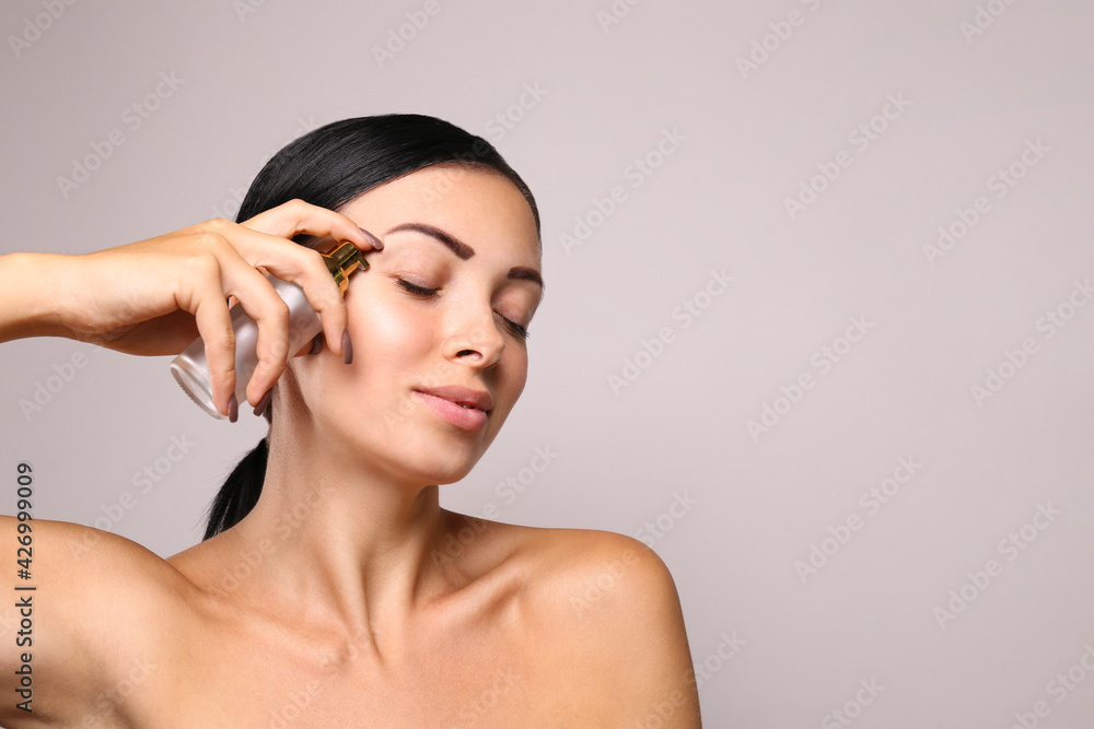 Portrait of young beautiful woman with perfectly clean face skin. Female with long brunette hair tied in ponytail applying moisturizing fluid. Close up, copy space, isolated background.