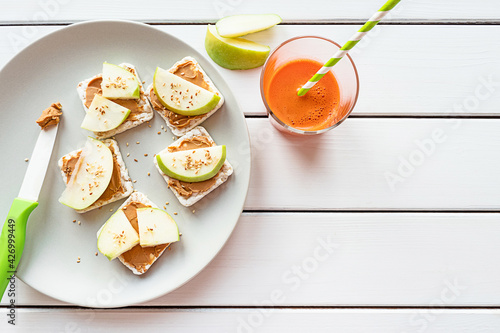 Healthy breakfast with peanut butter and apple sandwiches on rice cakes, carrot juice. Top view on white wooden background, copy space.