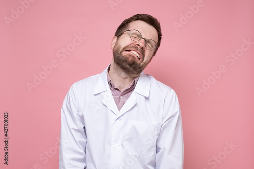 Young doctor in a white coat and round glasses is very tired, he is stressed, he closed eyes and made a miserable face.  © koldunova
