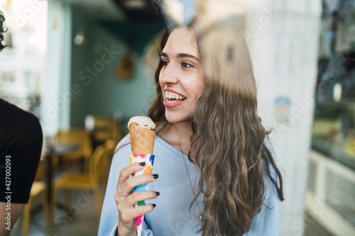 Chica joven tomando helado en cafeteria vista a través de un cristal