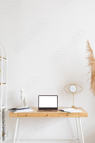 laptop wiith white screen on wooden table in home scandi interior. Stylish minimalistick workplace, copy space photo