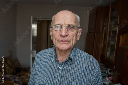 Raw portrait of older man in glasses standing in living room