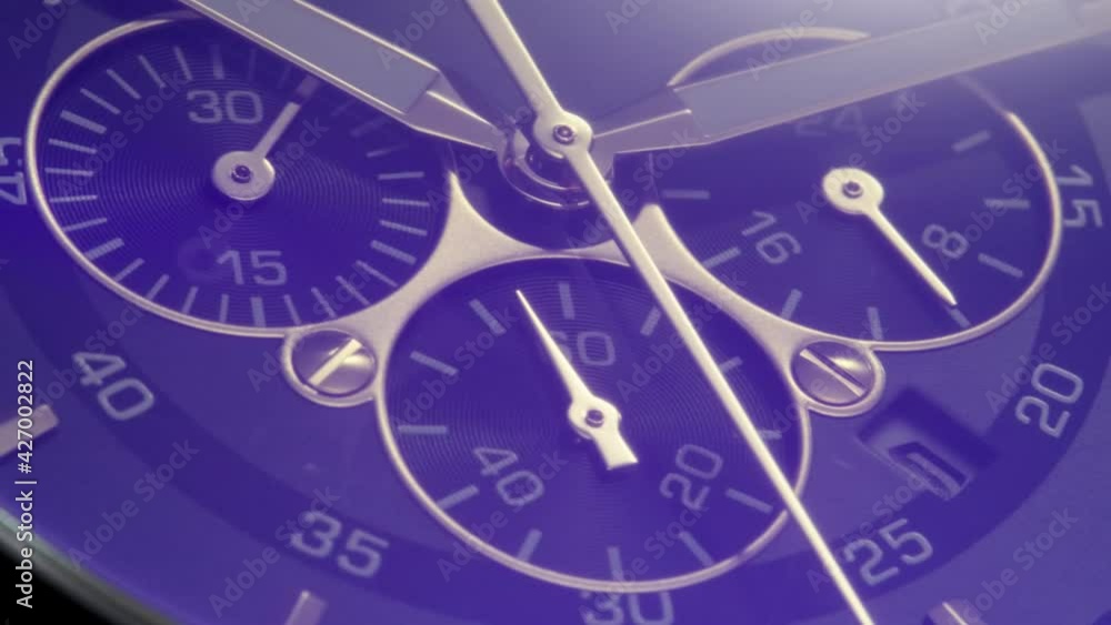 Luxury chronograph swiss watch with running second arrow and stopwatch turning on camera while light flash is passing by. Grey metallic body, blue flare and golden details on clockface. Closeup Luxury chronograph swiss watch with running second arrow and stopwatch turning on camera while light flash is passing by. Grey metallic body, blue flare and golden details on clockface. Closeup