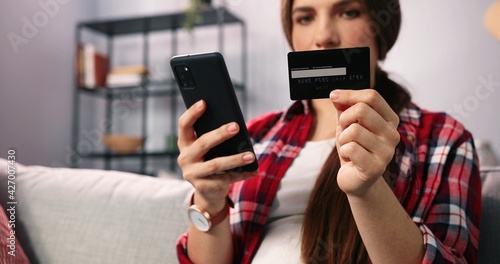 Let's buy this one. Young brunette woman sitting at the sofa at home, holding credit card and doing online shopping holding her cell phone. Impulse buying, online shopping, fast fashion, shopaholic