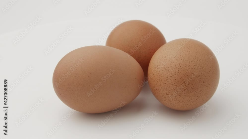 Chicken egg rotates on a white background. Close-up of an egg. Egg are rolling on the white table. Easter eggs background. Chicken egg rotates on a white background. Close-up of an egg. Egg are rolling on the white table. Easter eggs background.