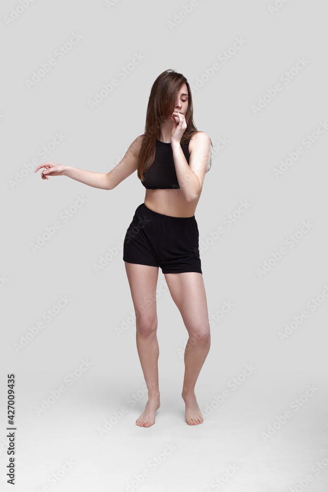 Young slim athletic girl, with long hair, in a black top and shorts, in the studio on a white background Young slim athletic girl, with long hair, in a black top and shorts, in the studio on a white background