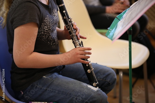 Close-up of a little girl in a black T-shirt and torn jeans playing the clarinet with her fingers on silver flaps in a music lesson at school.The concept of children's music education and development