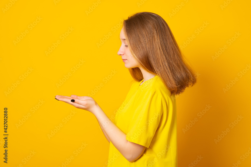 Cute teenager girl holds something in the palm. Young girl is holding something in her hand copy space for advertising on a yellow background. Cute teenager girl holds something in the palm. Young girl is holding something in her hand copy space for advertising on a yellow background.
