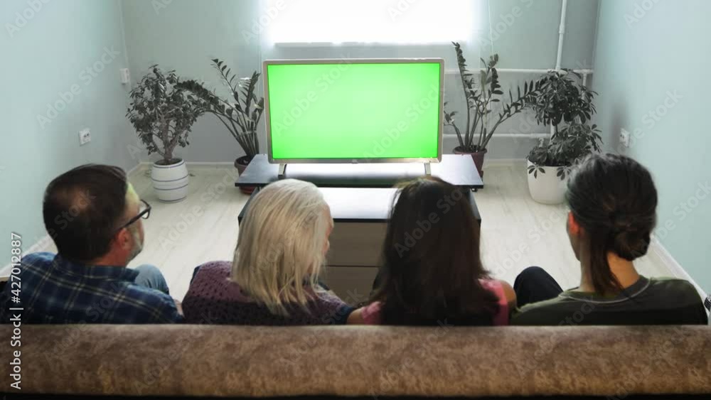 Family watching TV. Green screen. A family of two generations is sitting on the couch at home. In front of them is a green screen TV. Family watching TV. Green screen. A family of two generations is sitting on the couch at home. In front of them is a green screen TV.