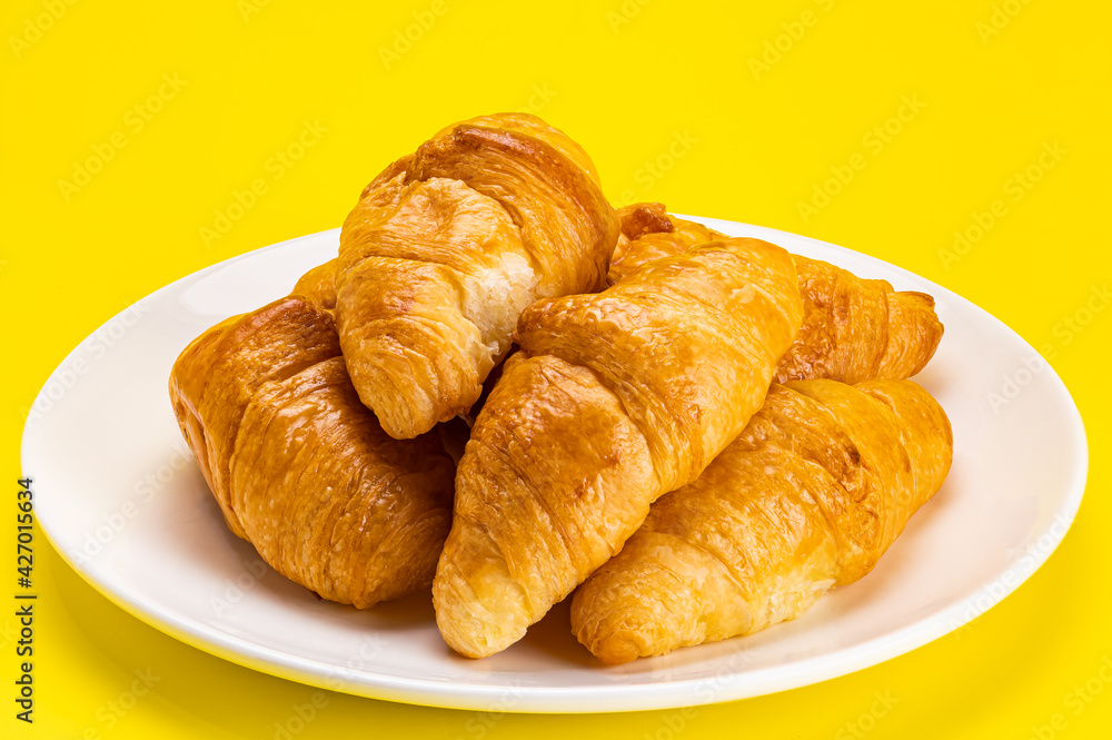 Pile of freshly baked croissants in white ceramic dish on yellow background with clipping path.