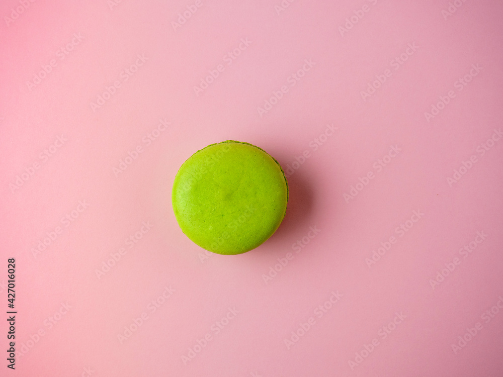 one macaroon cookie is green on a pink paper background. Minimalism, delicious dessert