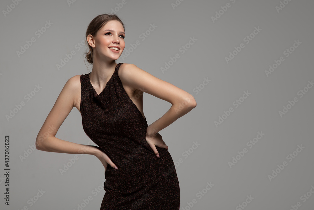 Smiling beautiful woman posing in a tight long dress. Gray background Smiling beautiful woman posing in a tight long dress. Gray background