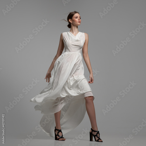 Fashion woman posing in white dress in full growth. Gray background
