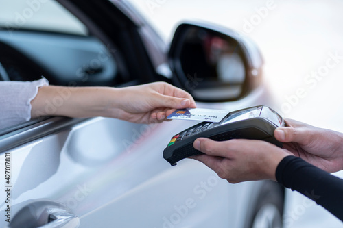 A woman sitting in a car, refueling, using a credit card, paying at the gas station. 