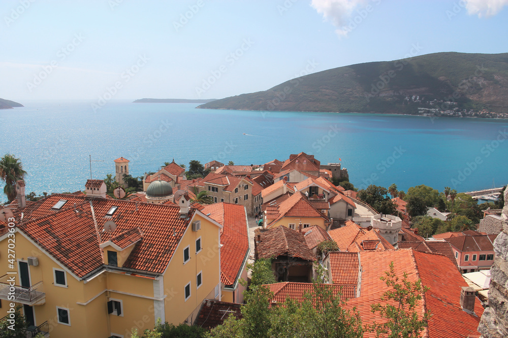 Top view of the orange tiled roofs of houses against the backdrop of azure sea water and beautiful mountains. Photography of Montenegro. Travel concept.