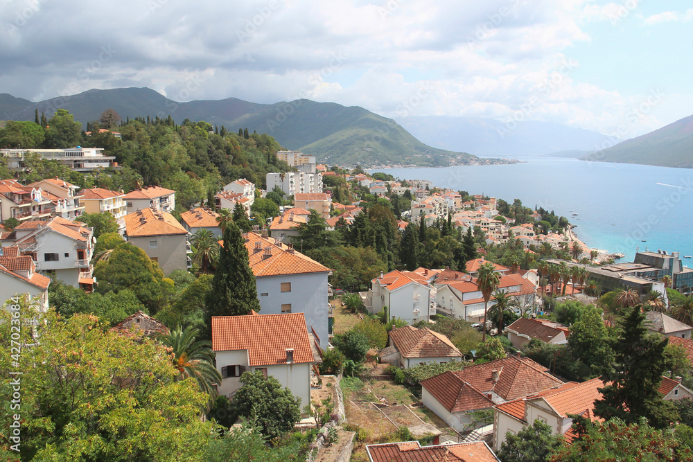 Top view of the orange tiled roofs of houses against the backdrop of azure sea water and beautiful mountains. Photography of Montenegro. Travel concept.