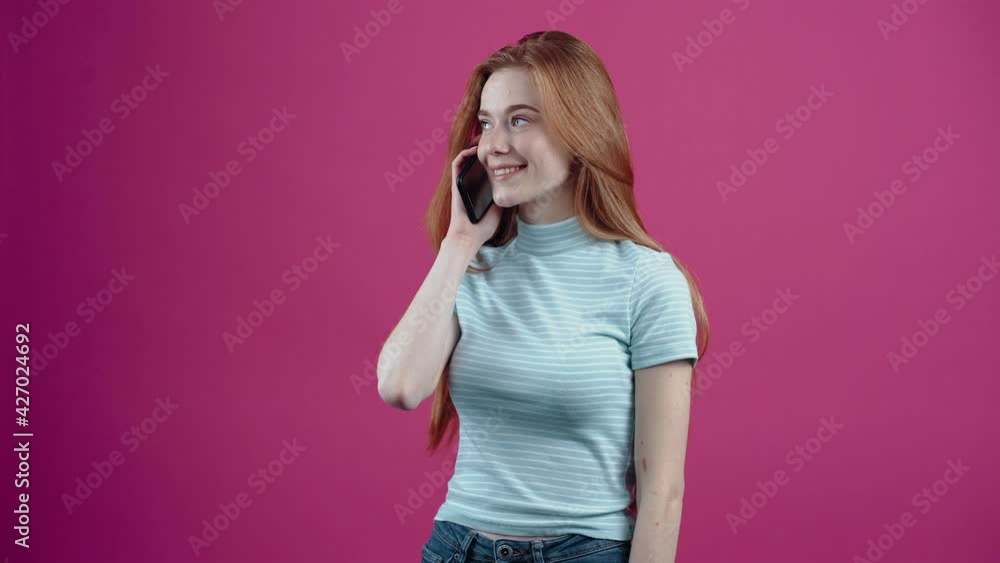The happy freckled young woman receives a call and speaks enthusiastically on the phone, in a pink casual T-shirt, isolated on a pink background. The concept of people's lifestyle The happy freckled young woman receives a call and speaks enthusiastically on the phone, in a pink casual T-shirt, isolated on a pink background. The concept of people's lifestyle