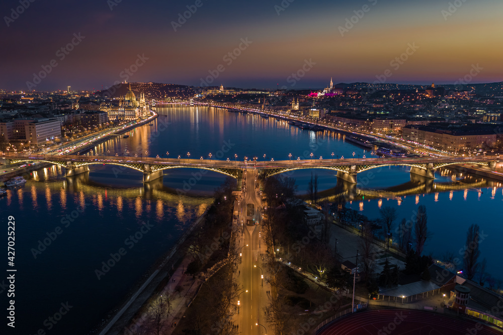 Fototapeta premium Budapest, Hungary - Aerial skyline panoramic view of illuminated Margaret Bridge at dusk. Parliament of Hungary, Szechenyi Chain Bridge and Buda Castle at background with clear golden and blue sky