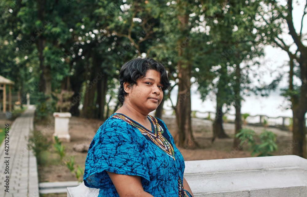 Portrait of a pensive looking middle aged Indian woman (Bengali ethnicity), standing near ledge of a garden-house, near Ganges river embankment. She is looking little exhausted. Portrait of a pensive looking middle aged Indian woman (Bengali ethnicity), standing near ledge of a garden-house, near Ganges river embankment. She is looking little exhausted.