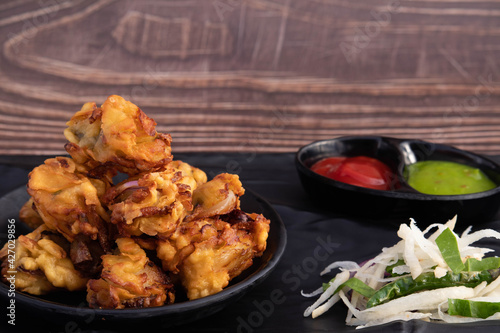 Onion Pakoda Also Known As Kanda Bhajji, Pyaj Ke Pakode, Pakoda, Pyaaj Pakore, Pakora, Pyaaz Bajji Is Enjoyed In Rainy Season Across North And South India. Served With Green Chutney And Ketchup Sauce