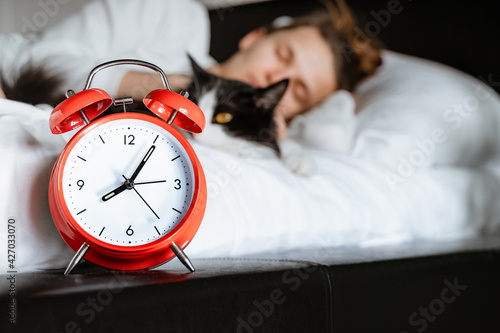 young millennial candid woman sleeping with pet cat on white blanket bed cozy at home in the bedroom. Close up of alarm clock, morning time, wake up, female healthy lifestyle concept.