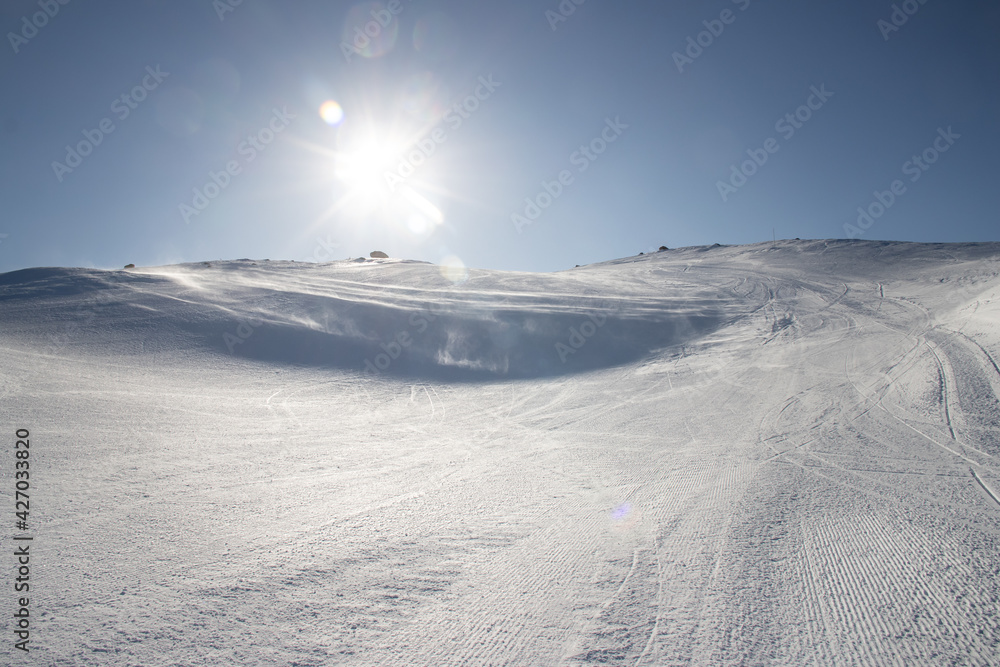 wind blowing snow over ski slope in the sun