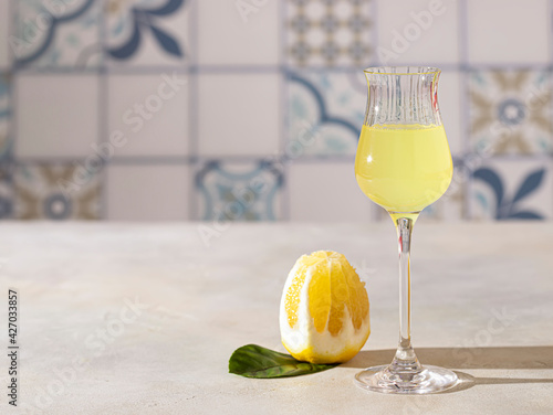 Fototapeta Naklejka Na Ścianę i Meble -  Limoncello, traditional Italian liquor on a light concrete background in the rays of the sun. Next to it is a yellow lemon, fresh citrus fruits.