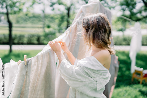 Woman Hanging Up Wet Laundry On Clothesline. The concept of unity girl with nature and the beginning of spring time with flowering trees. sunny day in village